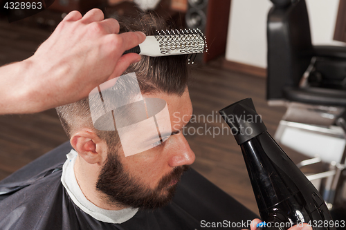 Image of The hands of barber making haircut to young man in barbershop