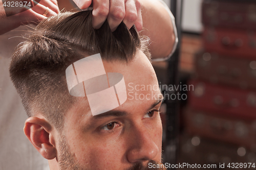 Image of The hands of barber making haircut to young man in barbershop