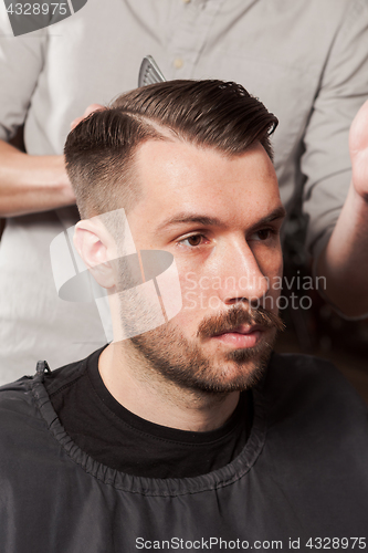 Image of The hands of barber making haircut to young man in barbershop