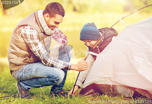 Image of happy father and son setting up tent outdoors