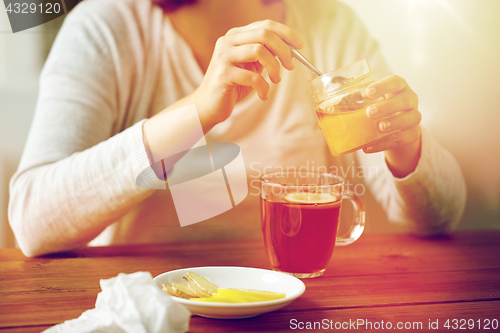 Image of close up of woman adding honey to tea with lemon