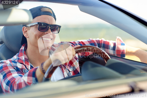 Image of happy young man in shades driving convertible car