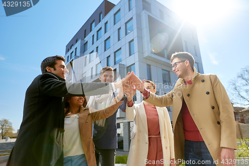 Image of group of happy people making high five in city