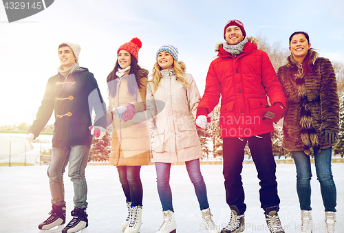 Image of happy friends ice skating on rink outdoors