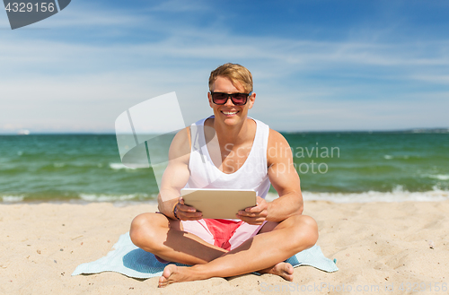 Image of happy smiling young man with tablet pc on beach