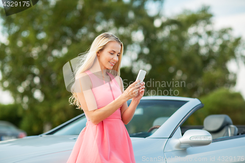 Image of young woman with smartphone at convertible car