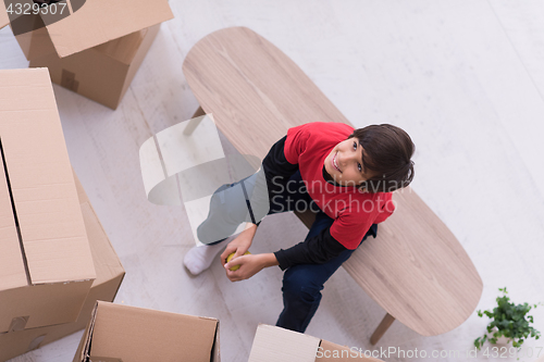 Image of boy sitting on the table with cardboard boxes around him top vie