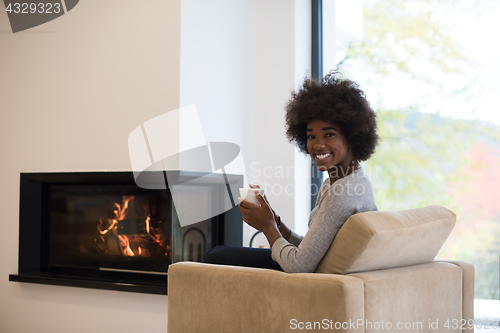 Image of black woman drinking coffee in front of fireplace