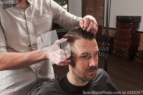 Image of The hands of barber making haircut to young man in barbershop