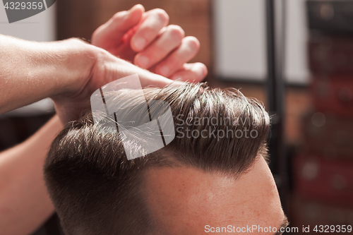 Image of The hands of barber making haircut to young man in barbershop