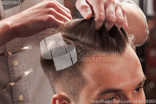 Image of The hands of barber making haircut to young man in barbershop