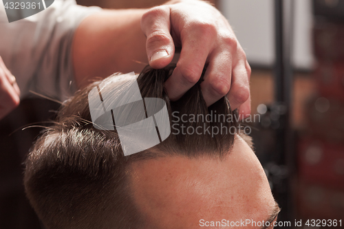 Image of The hands of barber making haircut to young man in barbershop