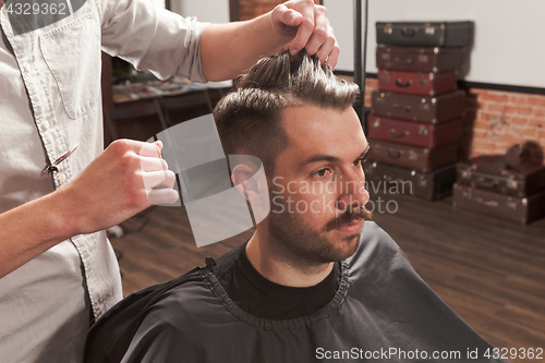 Image of The hands of barber making haircut to young man in barbershop