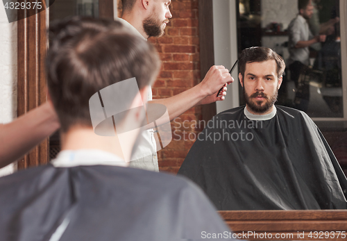 Image of Young handsome barber making haircut of attractive man in barbershop