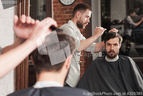 Image of Young handsome barber making haircut of attractive man in barbershop