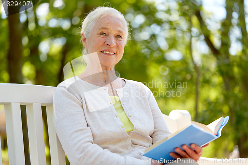 Image of happy senior woman reading book at summer park