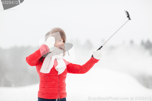 Image of happy woman with selfie stick outdoors in winter