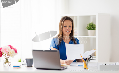 Image of happy woman with papers and laptop at office