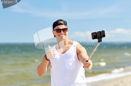 Image of man with smartphone selfie stick on summer beach