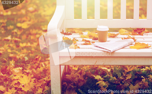 Image of newspaper and coffee cup on bench in autumn park