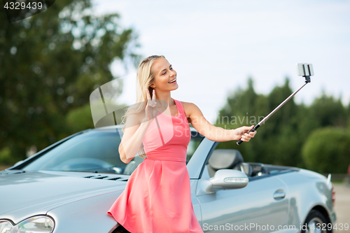 Image of woman taking picture by selfie stick at car
