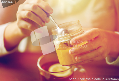 Image of close up of woman adding honey to tea with lemon