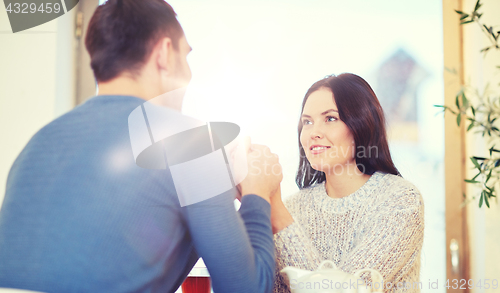 Image of happy couple with tea holding hands at restaurant