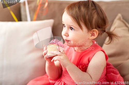 Image of happy baby girl eating cupcake on birthday party