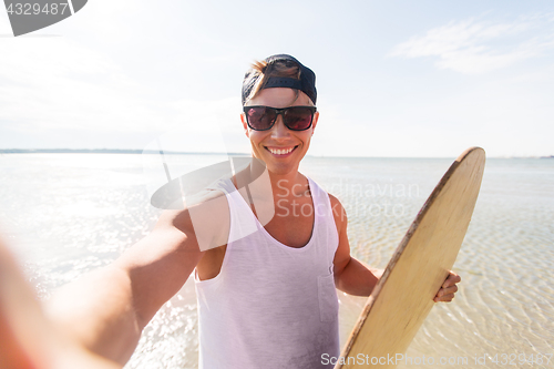 Image of happy young man with skimboard on summer beach