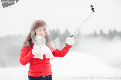 Image of happy woman with selfie stick outdoors in winter