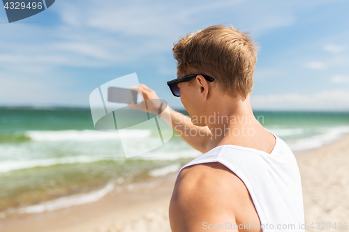 Image of man with smartphone photographing on summer beach