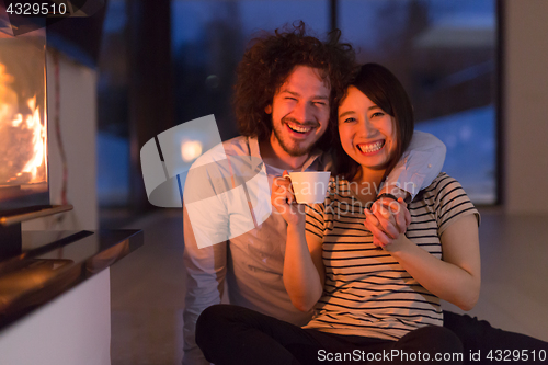 Image of happy multiethnic couple sitting in front of fireplace