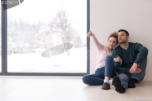 Image of young couple sitting on the floor near window at home