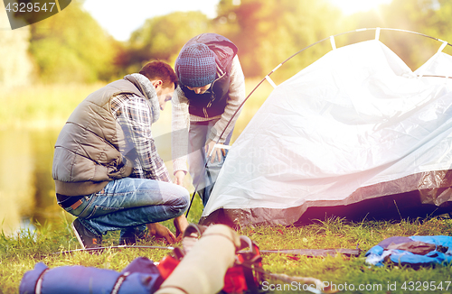 Image of happy father and son setting up tent outdoors