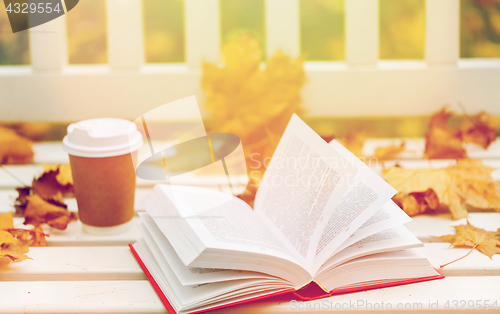 Image of open book and coffee cup on bench in autumn park