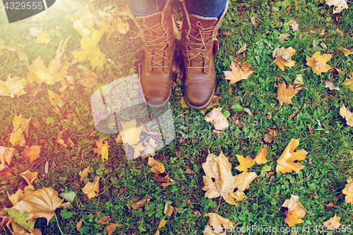 Image of female feet in boots and autumn leaves on grass