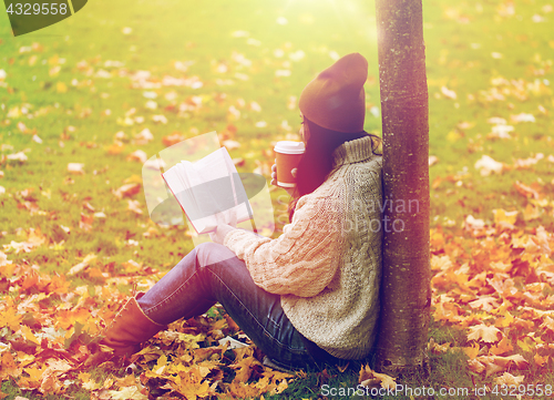 Image of woman with book drinking coffee in autumn park