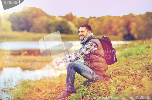 Image of smiling man with backpack resting on river bank