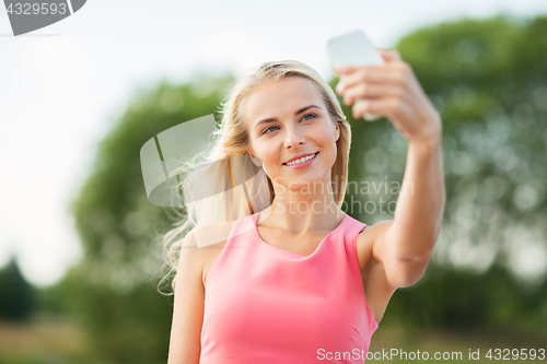 Image of happy woman taking selfie with smartphone outdoors