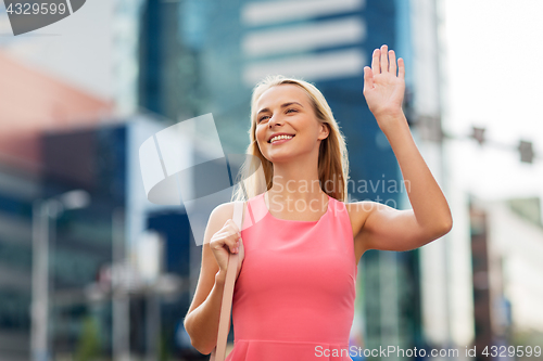 Image of happy young woman waving hand on city street