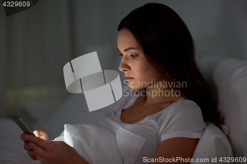 Image of young woman with smartphone in bed at night