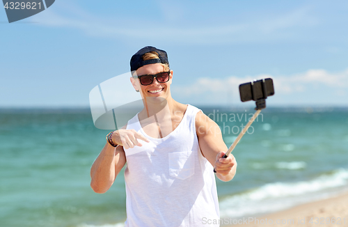 Image of man with smartphone selfie stick on summer beach