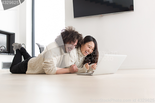 Image of young multiethnic couple using a laptop on the floor