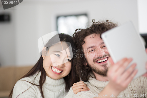 Image of multiethnic couple using tablet computer in front of fireplace