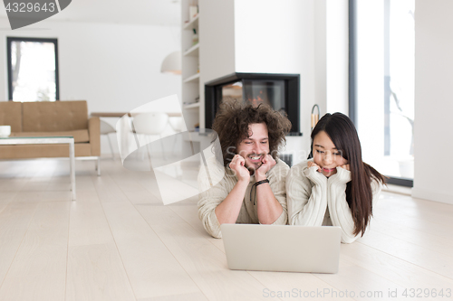 Image of young multiethnic couple using a laptop on the floor