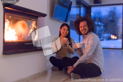 Image of happy multiethnic couple sitting in front of fireplace