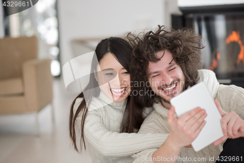 Image of multiethnic couple using tablet computer in front of fireplace