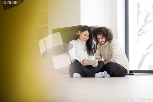 Image of multiethnic couple using tablet computer in front of fireplace