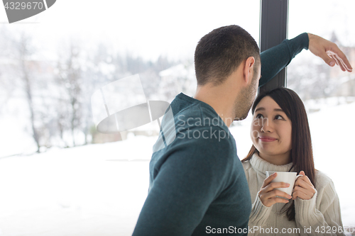 Image of multiethnic couple enjoying morning coffee by the window