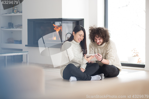 Image of multiethnic couple using tablet computer in front of fireplace